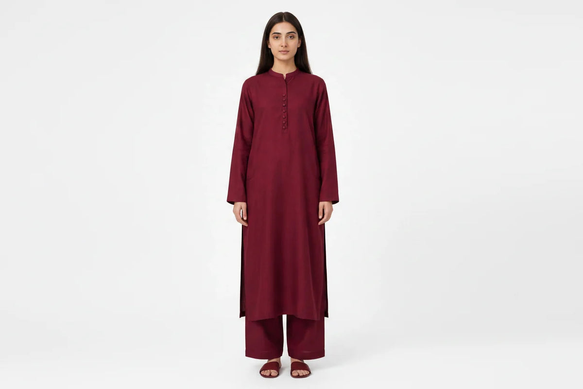 A woman modeling a long-sleeved maroon kurta and matching palazzo pants set against a plain white studio background.